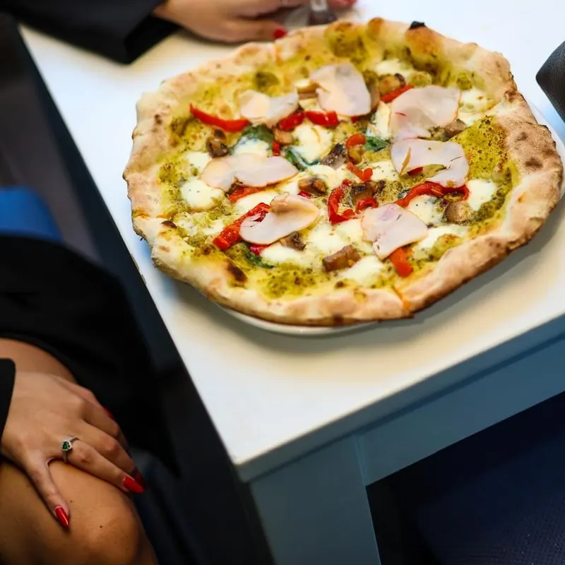 Pesto pizza with chicken and red peppers next to a glass of red wine