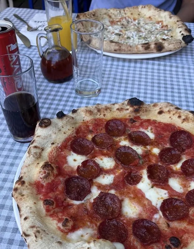 A pepperoni pizza with a cola on a blue checked tablecloth