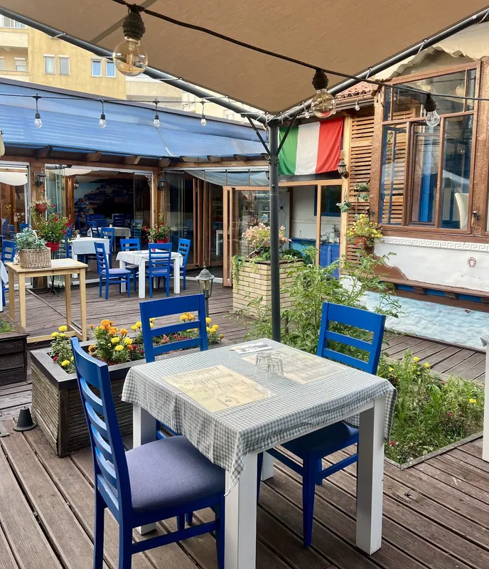 The covered terrace with blue chairs, checked tablecloths and an Italian flag