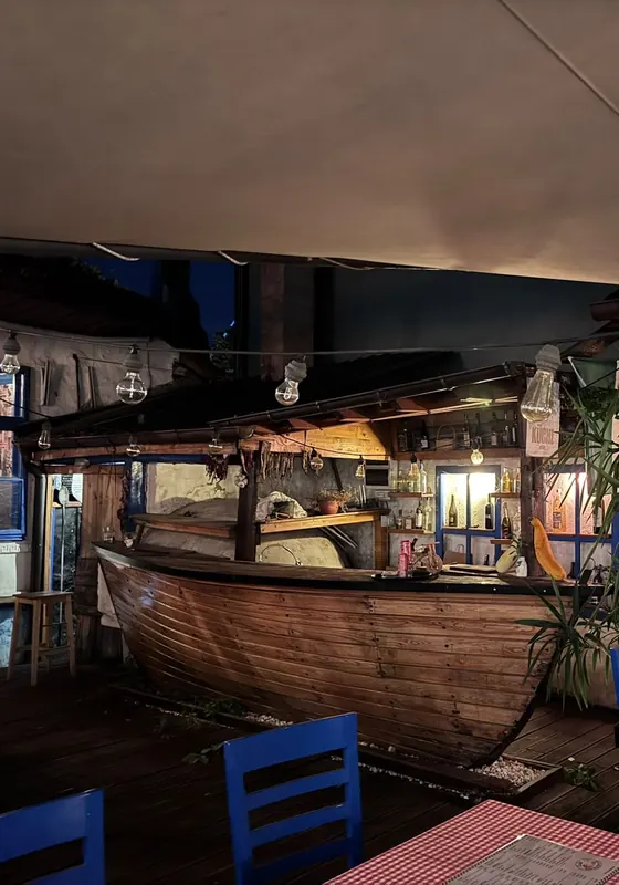 The bar built into an old wooden boat, with blue chairs and red checked tables